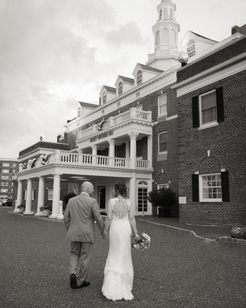 Elegant bride and groom walk in front of the historic Molly Pitcher Inn in Red Bank, NJ by wedding photographer Laura Billingham