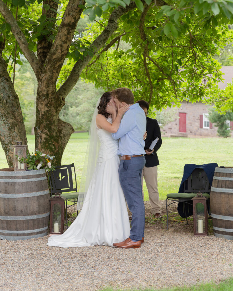 bride and groom share their first kiss in a rustic chic wedding ceremony at Woolverton Inn, photography by Laura Billingham