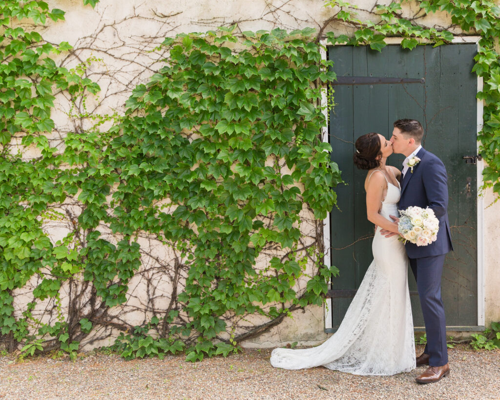 an elegant bride and groom kiss by a green door at Bridgeton House on the Delaware by Laura Billingham Photography