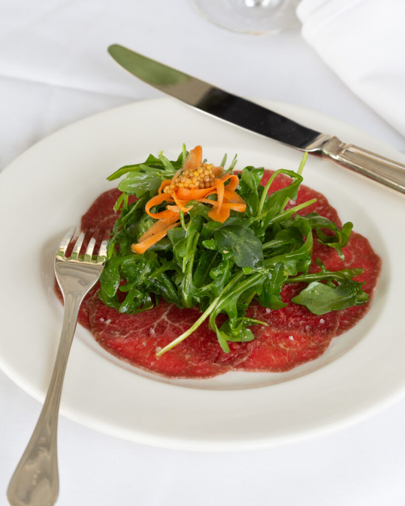 Close up photo of beef carpacio with arugula salad and carrot shreds on top prepared by Chef Jon McCain at Cascade restaurant at Durham Springs, photographed by Laura Billingham Photography