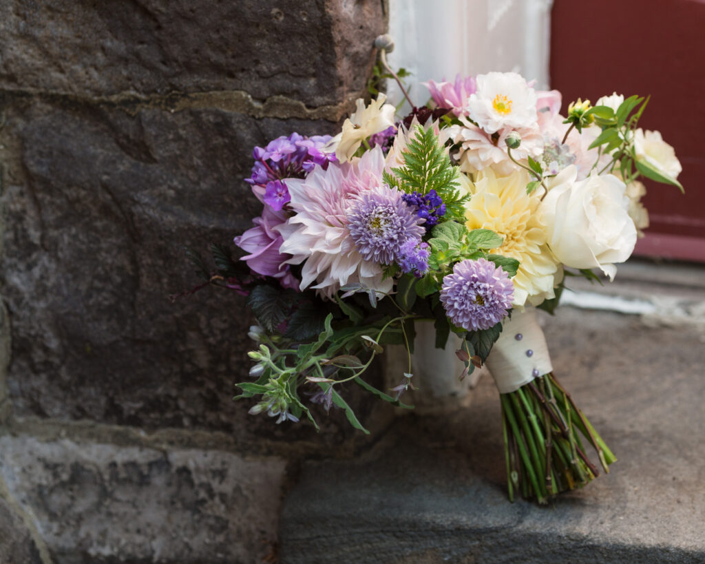 Fall bridal bouquet with purple, ivory, white and green flowers against a gothic stone church wall at Flemington Presbyterian Church in Flemington, NJ by Laura Billingham Photography