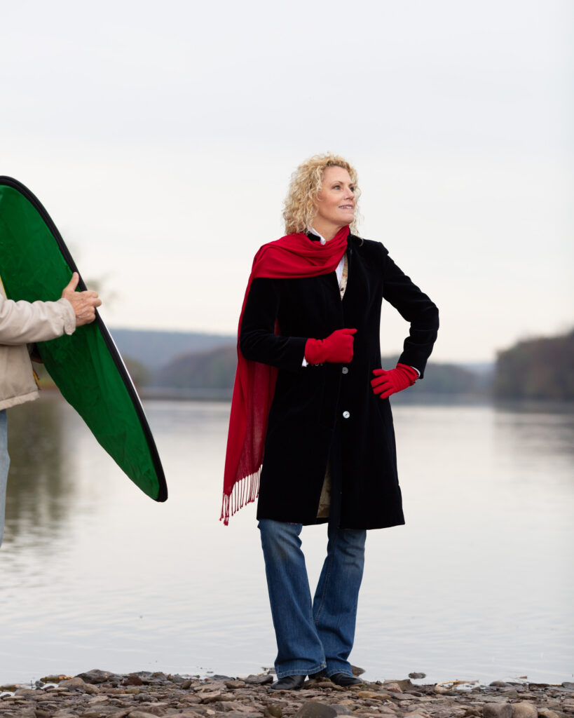 Behind the scenes photograph of Laura Townsend Barnes, author, conservationist, restaurateur and race car driver on the banks of the Delaware River in Frenchtown, NJ photographed on location for River Towns Magazine by Laura Billingham Photography