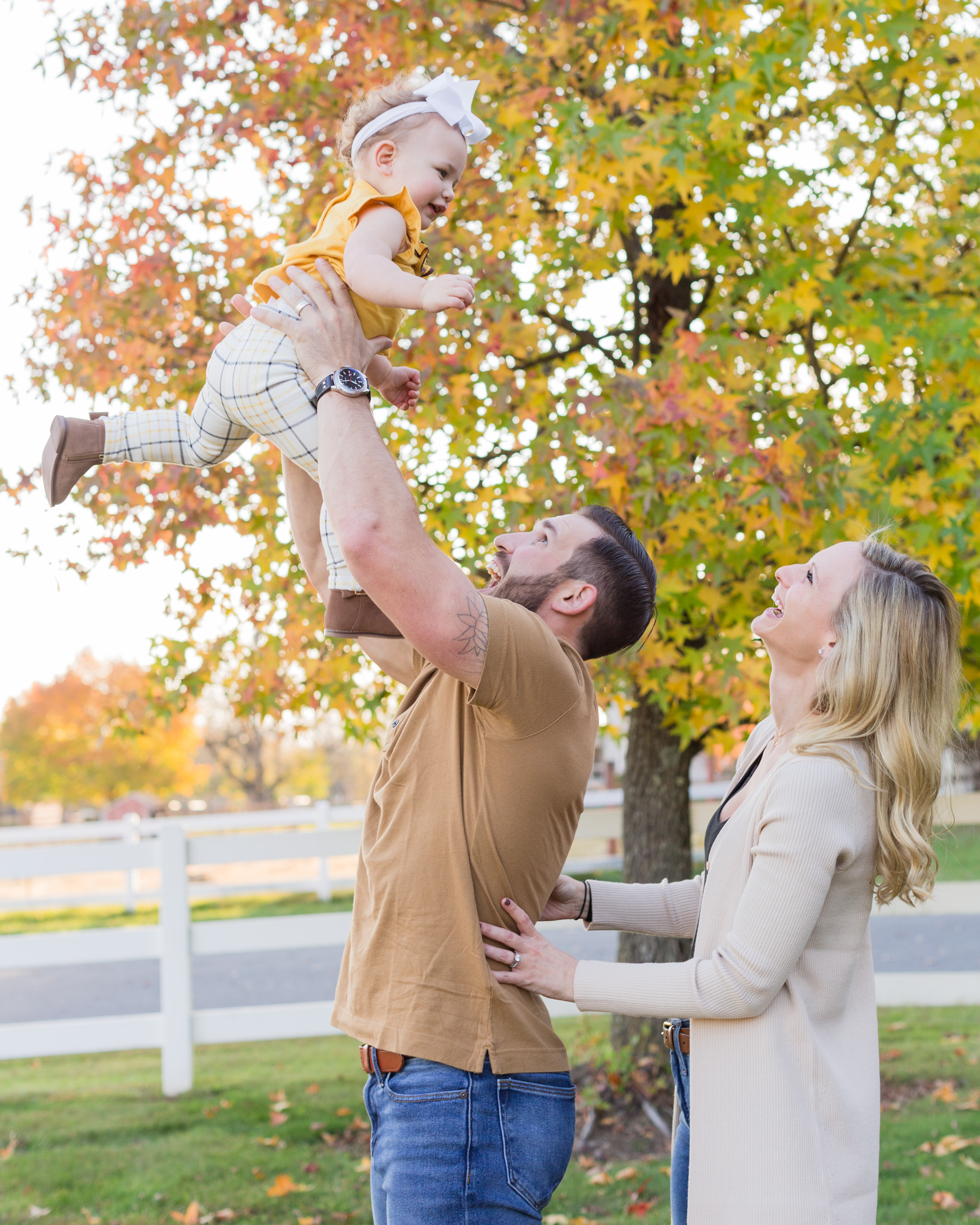 Fall portrait of a dad tossing baby daughter in the air while mom hugs him and laughs in Whitehouse Station, NJ