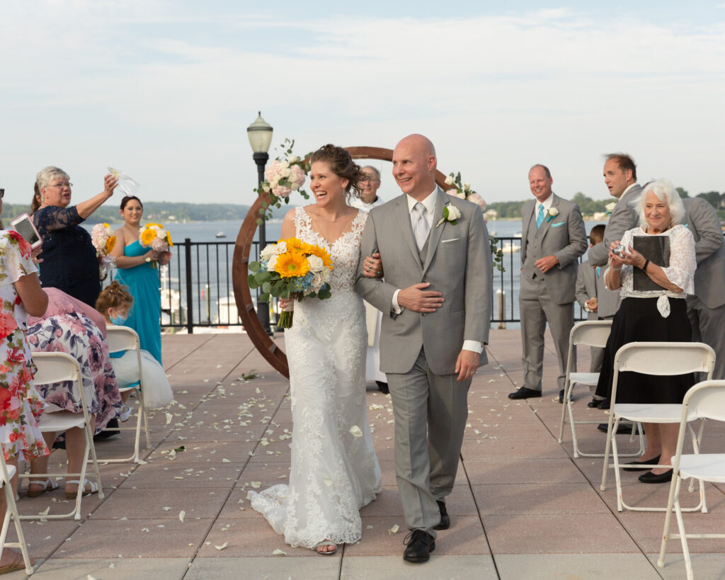 Jubilant bride and groom walking away from the altar after saying their vows during a summer outdoor wedding ceremony at the Molly Pitcher Inn in Red Bank, NJ photographed by Laura Billingham