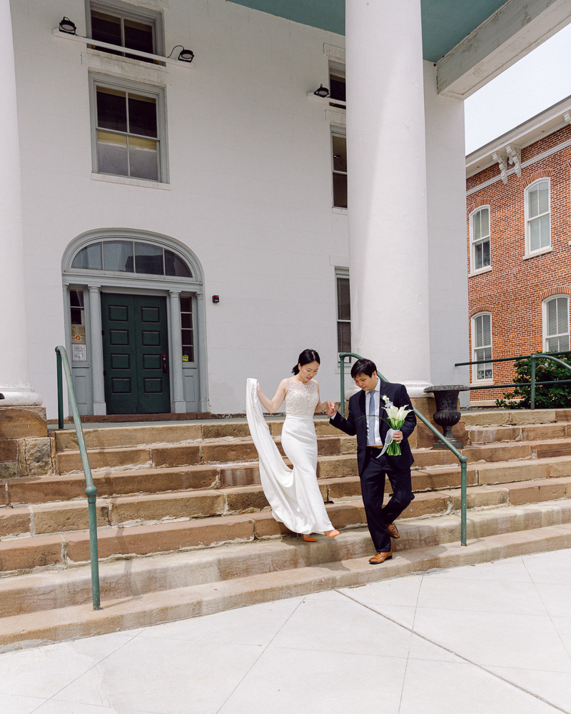 Bride and groom in elegant attire descend the Hunterdon County Courthouse steps after their elopement ceremony