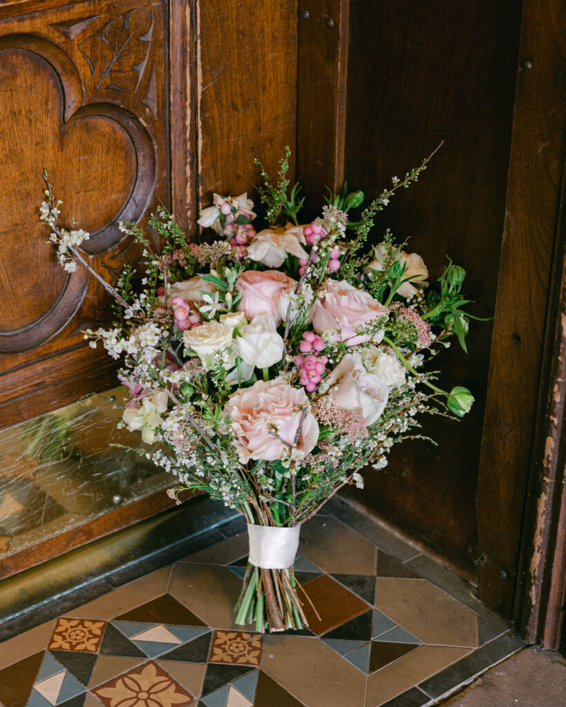 Lush spring bridal bouquet of pink and ivory wildflowers next to an ornate historic door on a richly tiled entryway at the Sayre Mansion in Bethlehem, PA