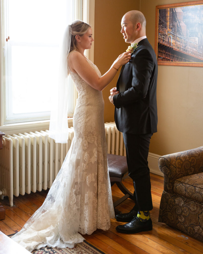 Elegant bride adjusts groom's tie while getting ready before their wedding ceremony at the Sayre Mansion in Bethlehem, PA 