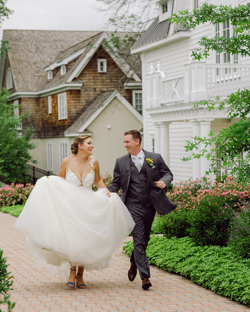 Energetic bride and groom in elegant attire run and laugh at the Coach House at the Ryland Inn in Whitehouse Station, NJ by Laura Billingham Photography