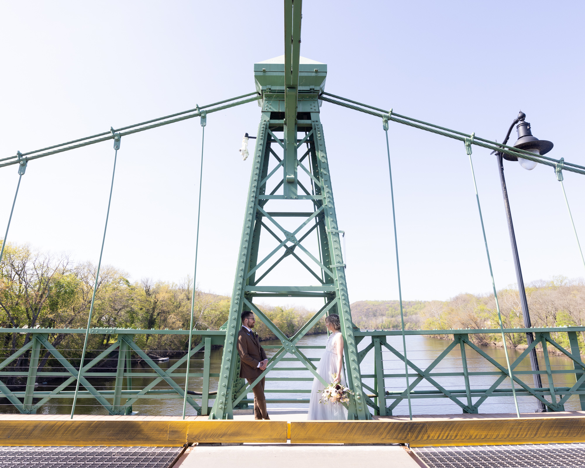 Elegant bride and groom lean against the Riegelsville PA bridge after their micro wedding