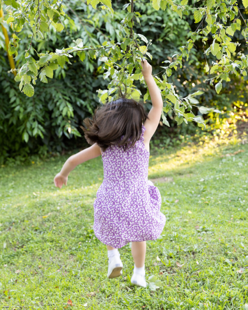 portrait of a 6 year old girl in a purple dress jumping with joy with her back turned from camera