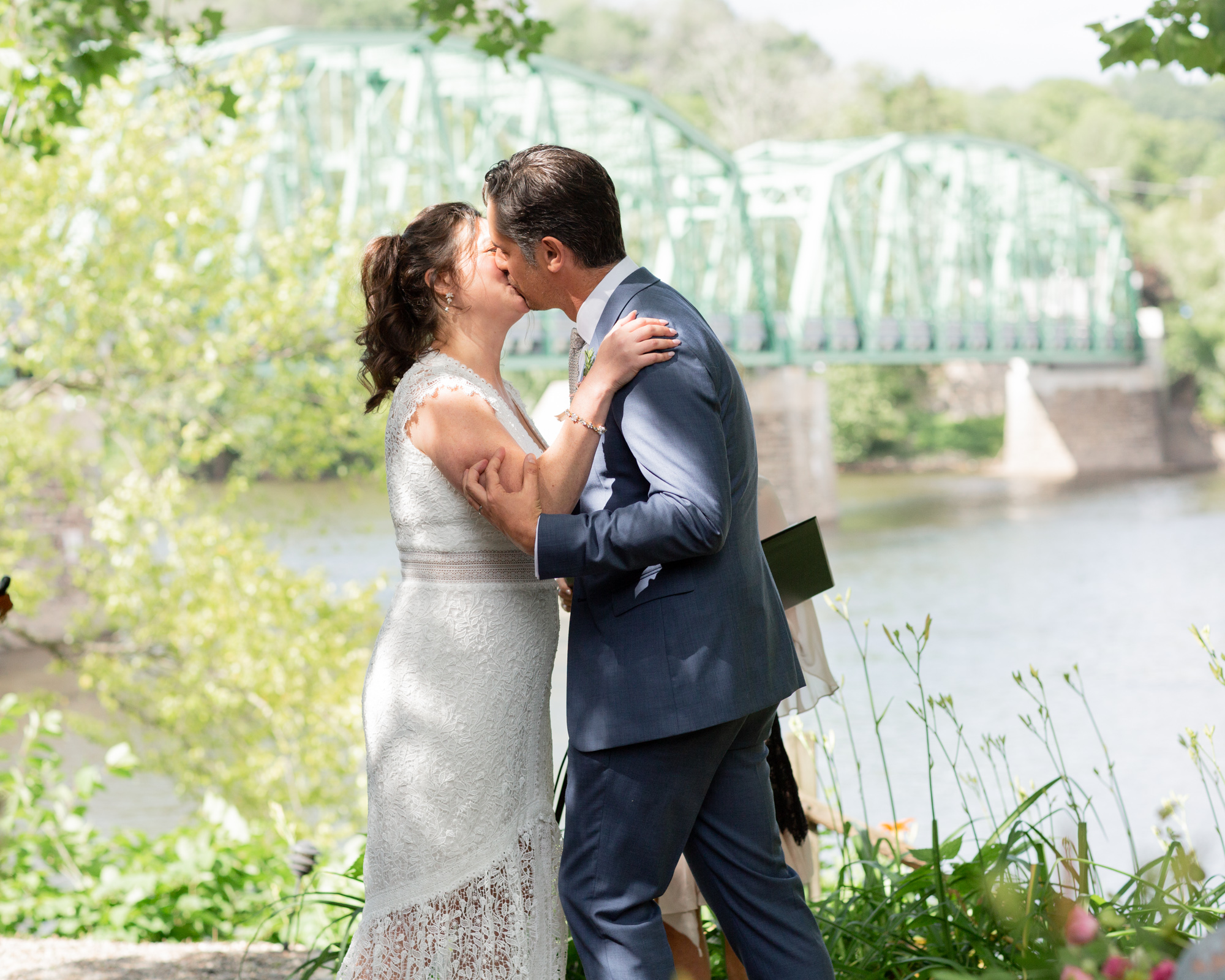 Stylish couple kiss at their wedding ceremony over looking the Milford Bridge at Bridgeton House on the Delaware in Bucks County, PA