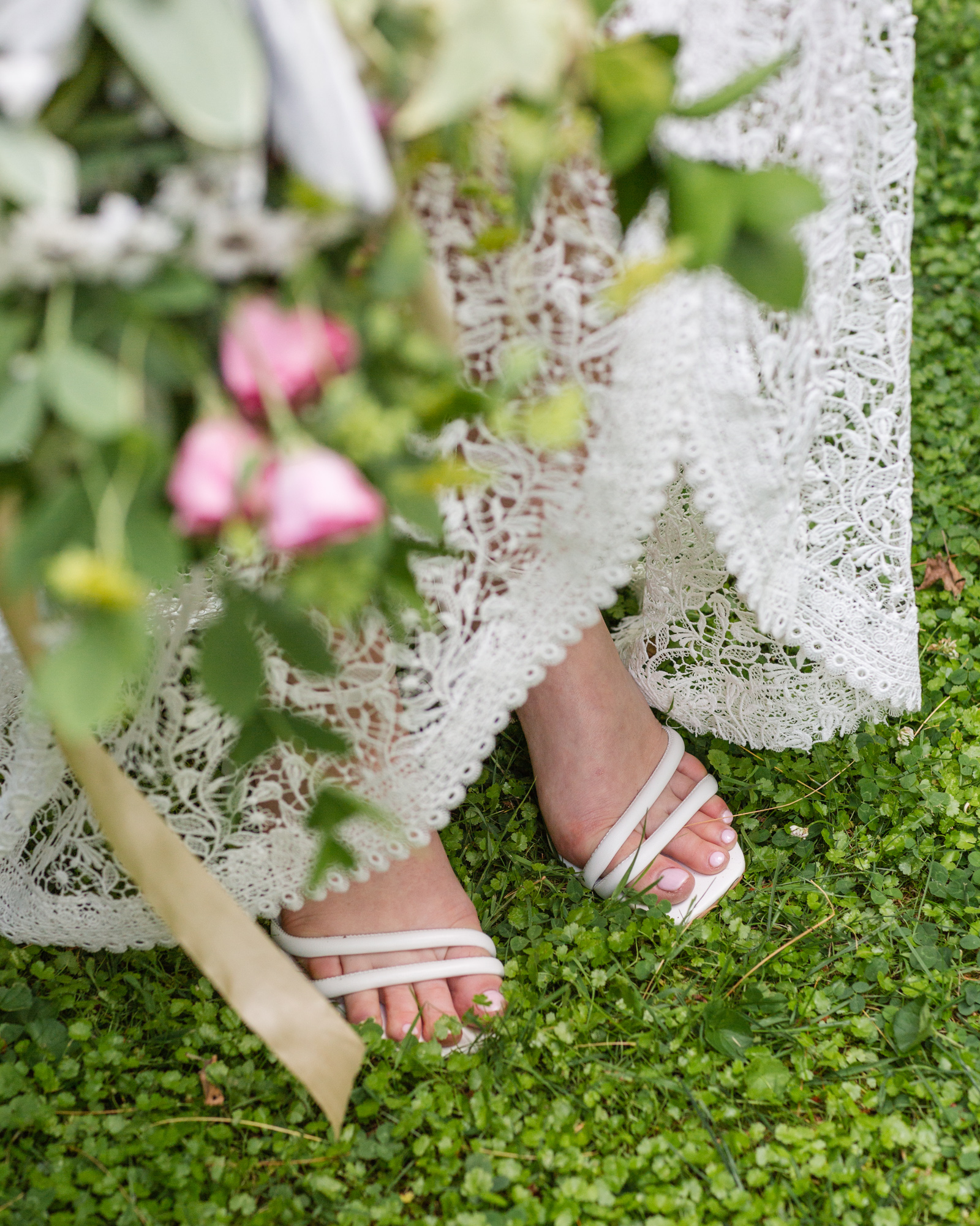 Detail of bride's stylish lace wedding gown and sandals in lush green grass at Bridgeton House on the Delaware in Bucks County, PA