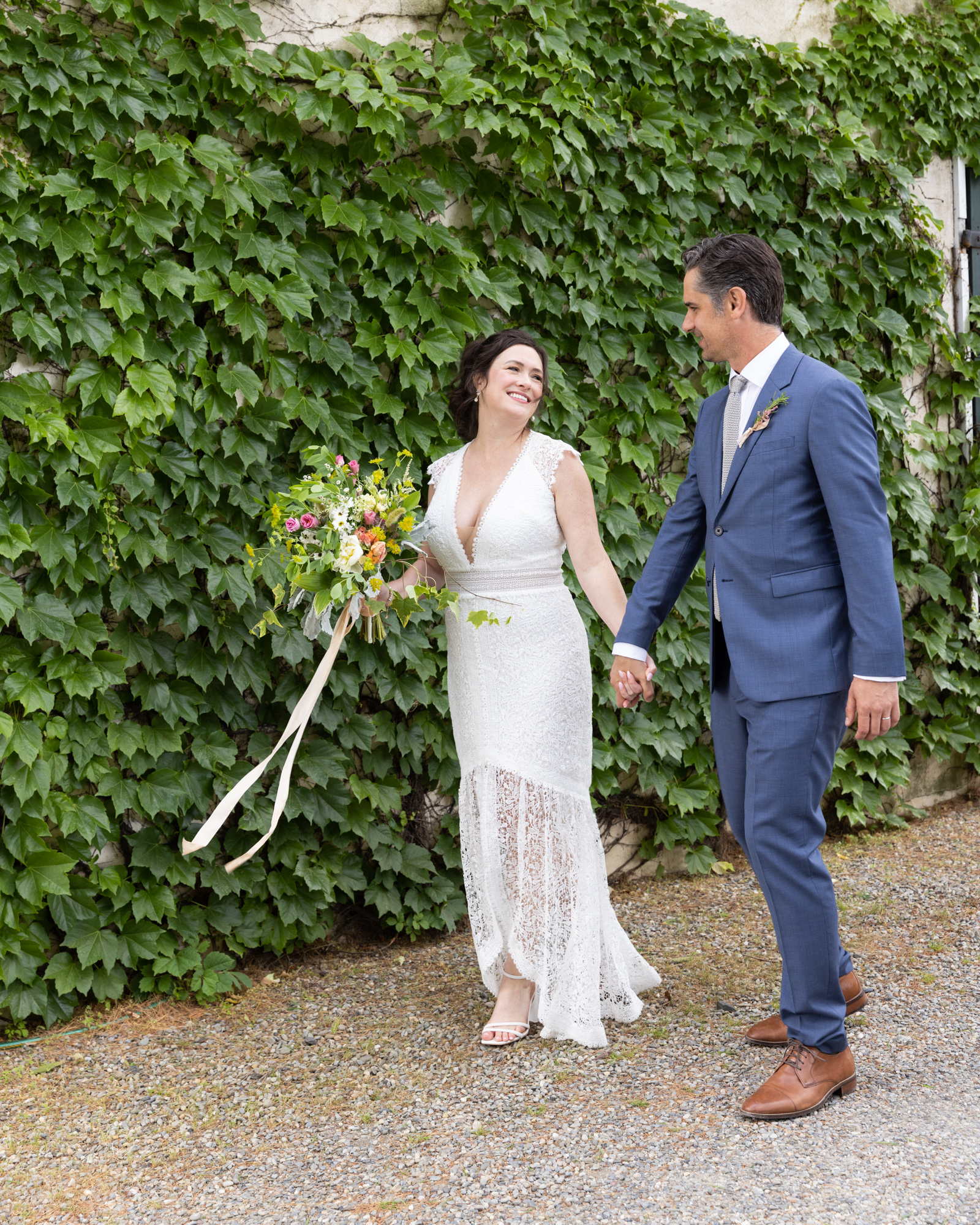 Elegant bride and groom walk holding hands near ivy covered wall at Bridgeton House on the Delaware in Bucks County, PA