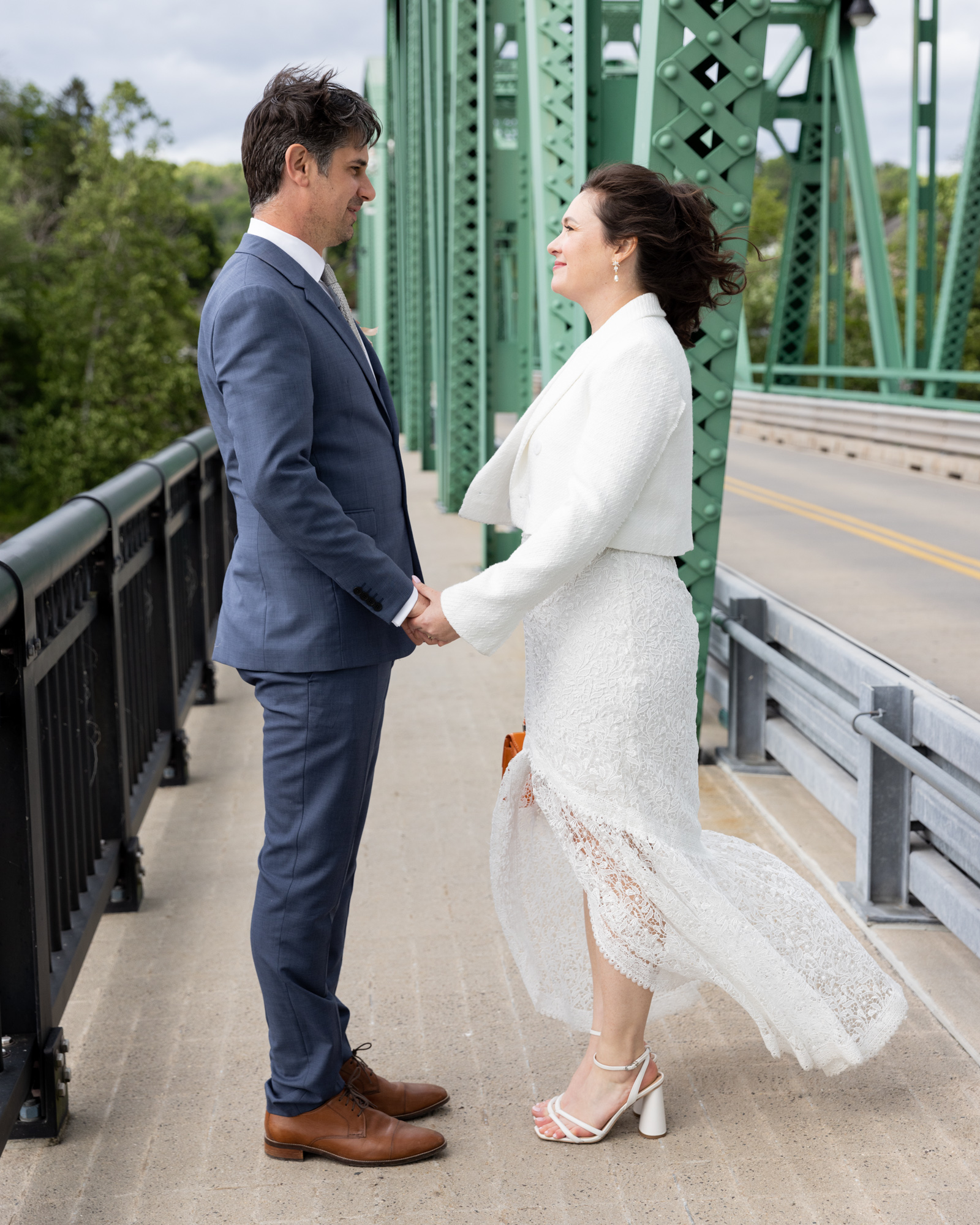Stylish couple facing each other on the Milford Bridge in Bucks County, PA. The wind is blowing the brides hair and gown while they hold hands and look at each other