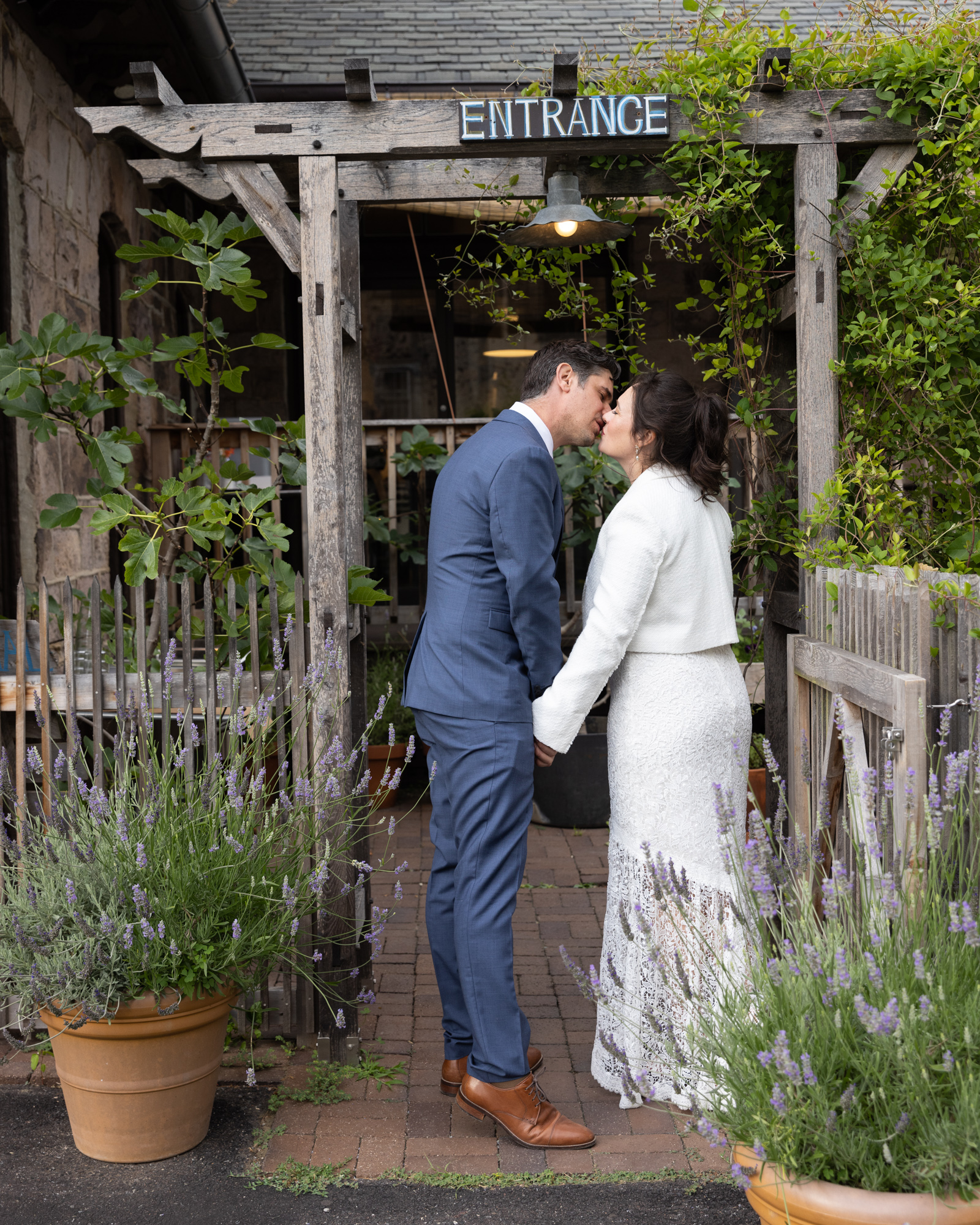 Stylish bride and groom kiss under the garden gate at Canal House Station in Milford NJ just before entering their wedding reception