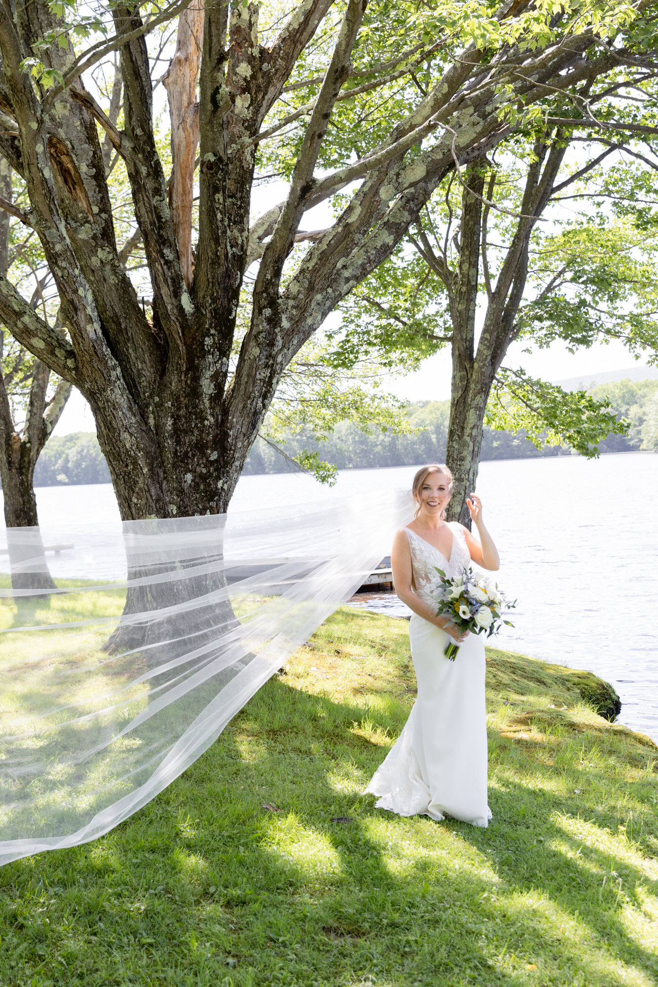 An elegant bride with her veil blowing in the breeze near a lake at Mountain Springs Lake Resort in the Poconos in Reeders, PA