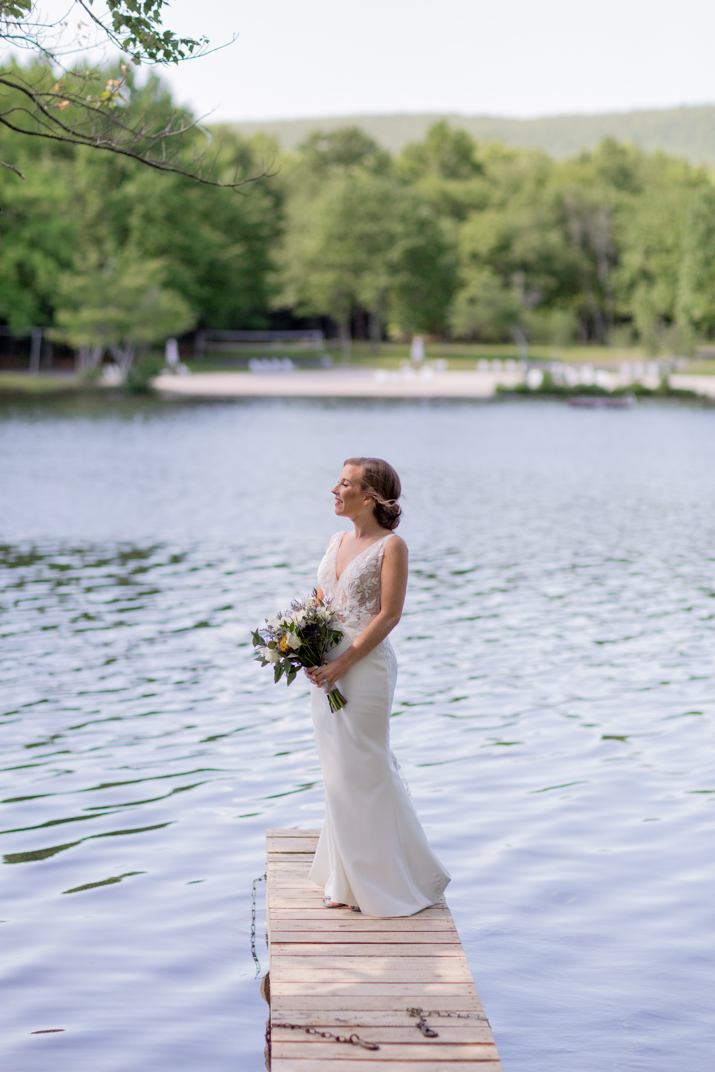 A serene bride holding a bouquet stands on a dock in the lake at Mountain Springs Lake Resort in the Poconos in Reeders, PA