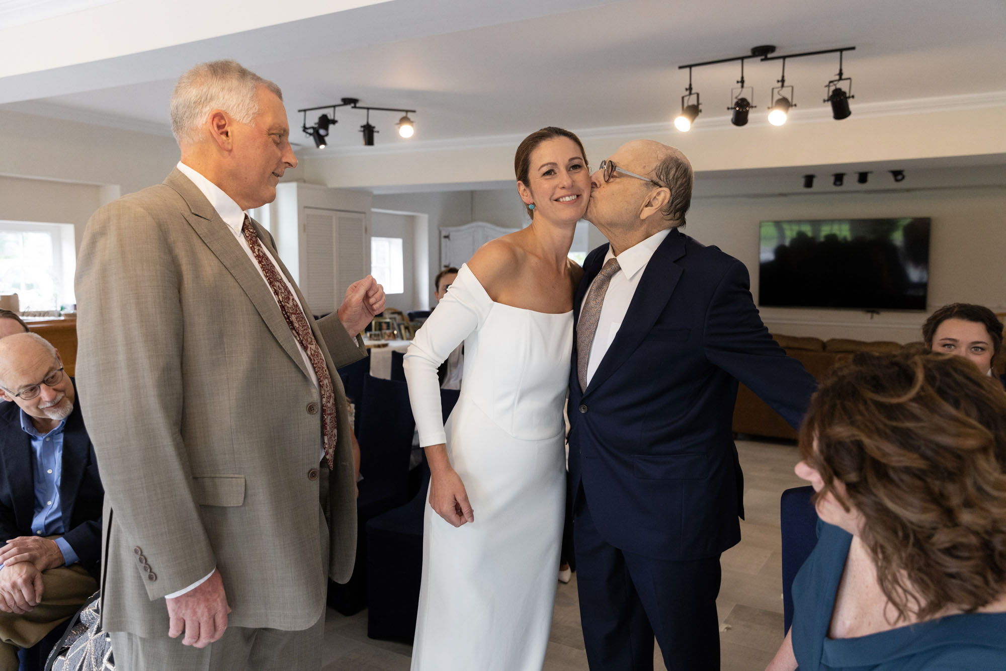 Elegant bride gets a kiss from her dad as her step father looks on during her wedding ceremony at Chimney Hill Estate Inn in Lambertville, NJ
