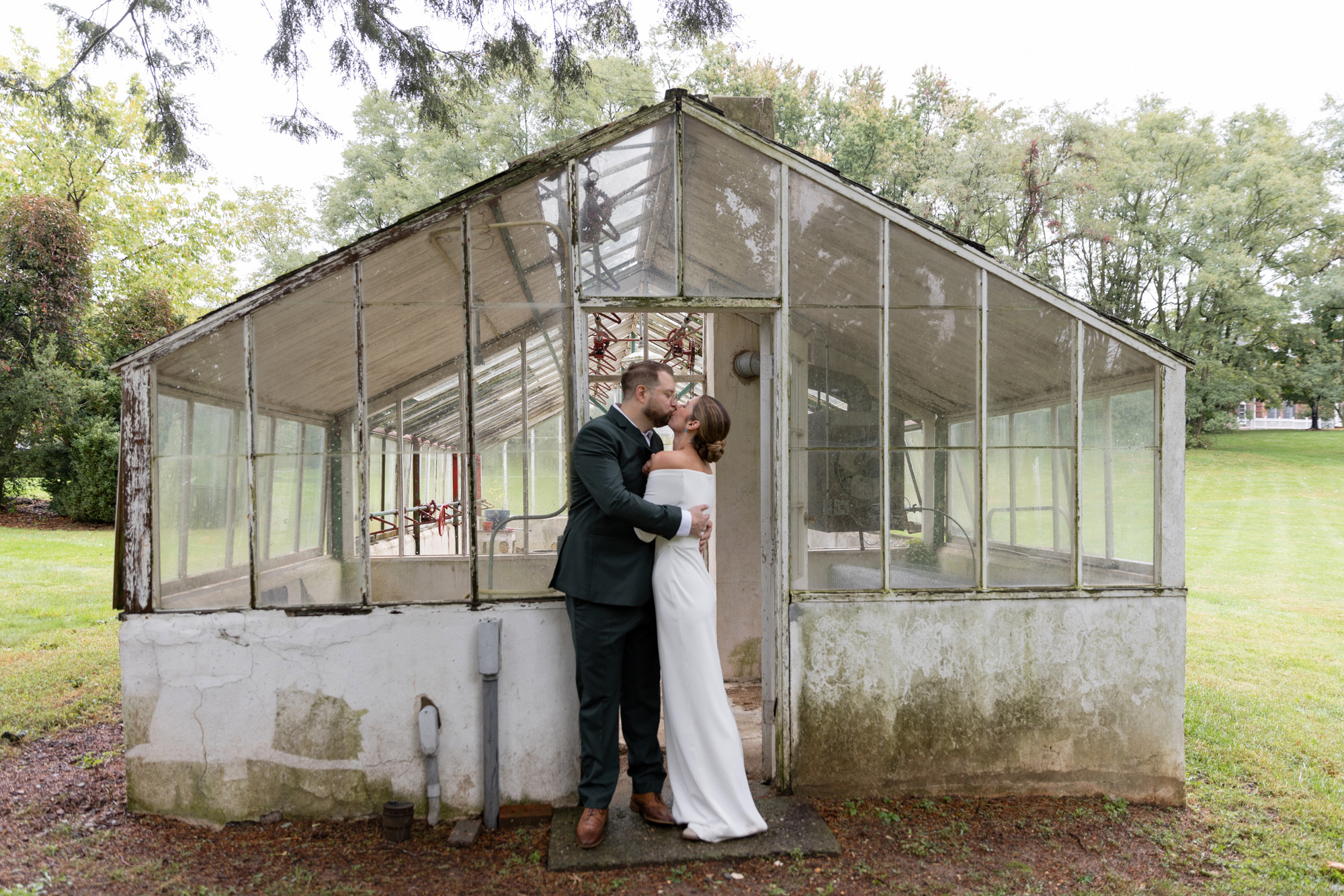 Elegant bride and groom embrace in front of a greenhouse after their wedding ceremony at Chimney Hill Estate Inn in Lambertville, NJ