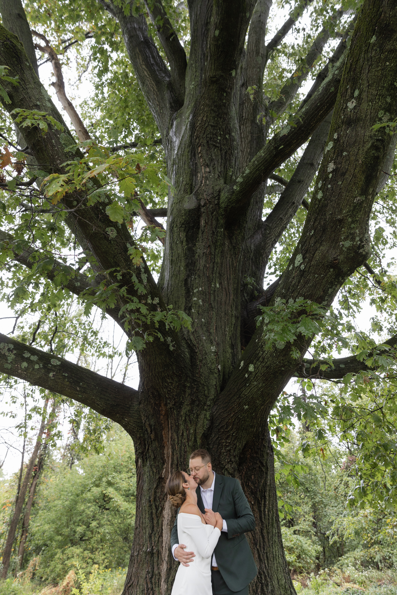 an elegant bride and groom kiss under a towering tree after their wedding ceremony at Chimney Hill Estate Inn in Lambertville, NJ