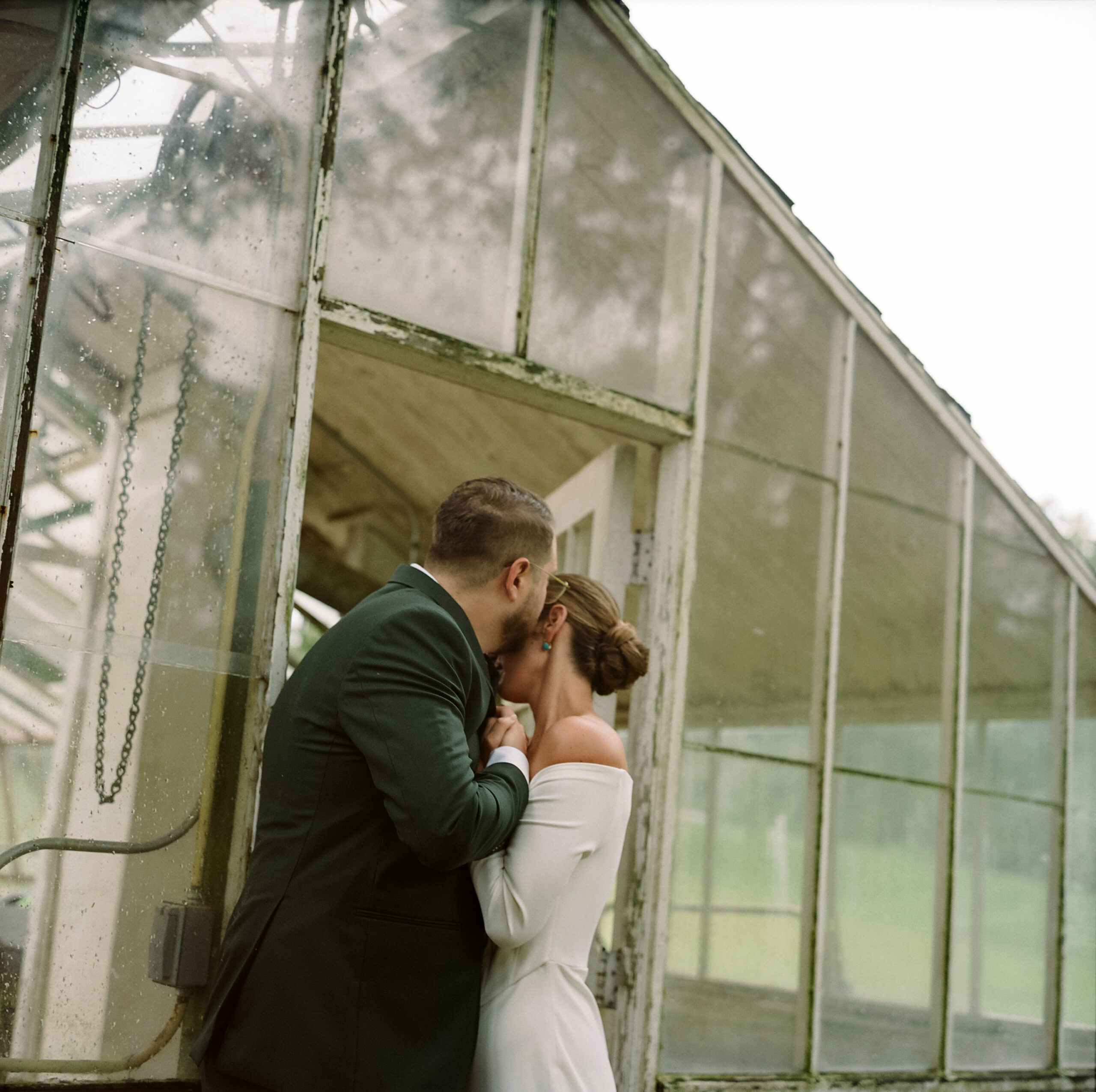 Groom sweetly kisses the forehead of the bride in front of a greenhouse after their wedding ceremony at Chimney Hill Estate Inn in Lambertville, NJ