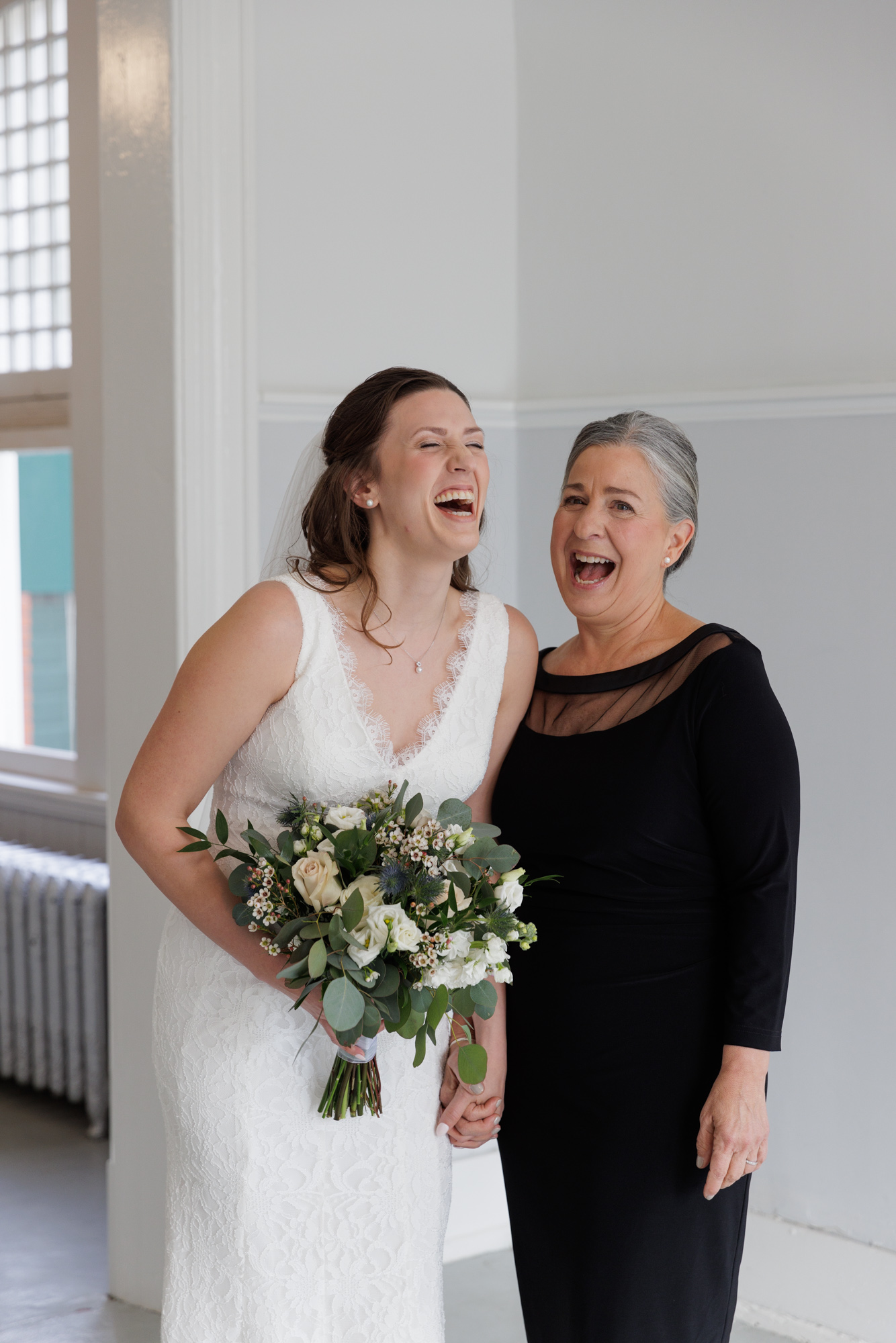 Elegant mother of the bride and bride laugh during a portrait session at a wedding at Old City Hall in Bordentown, NJ