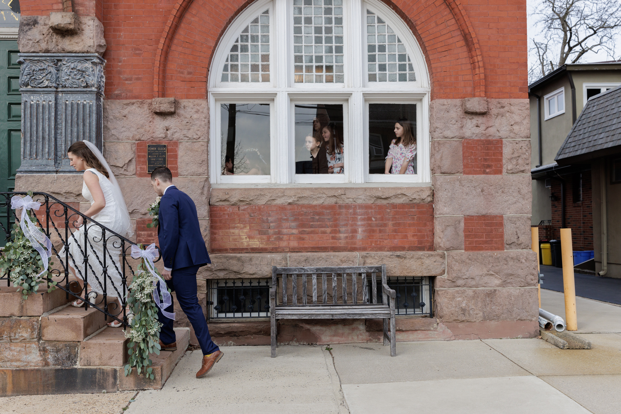 Adorable children at a wedding look out a window as the bride and groom walk by in front of Old City Hall in Bordentown, NJ 