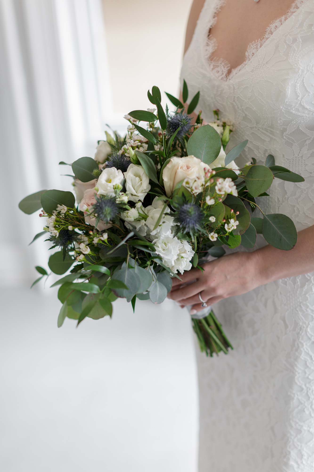 Detail of a bride holding a bouquet of elegant white flowers and green foliage before a winter wedding ceremony at Old City Hall in Bordentown, NJ 