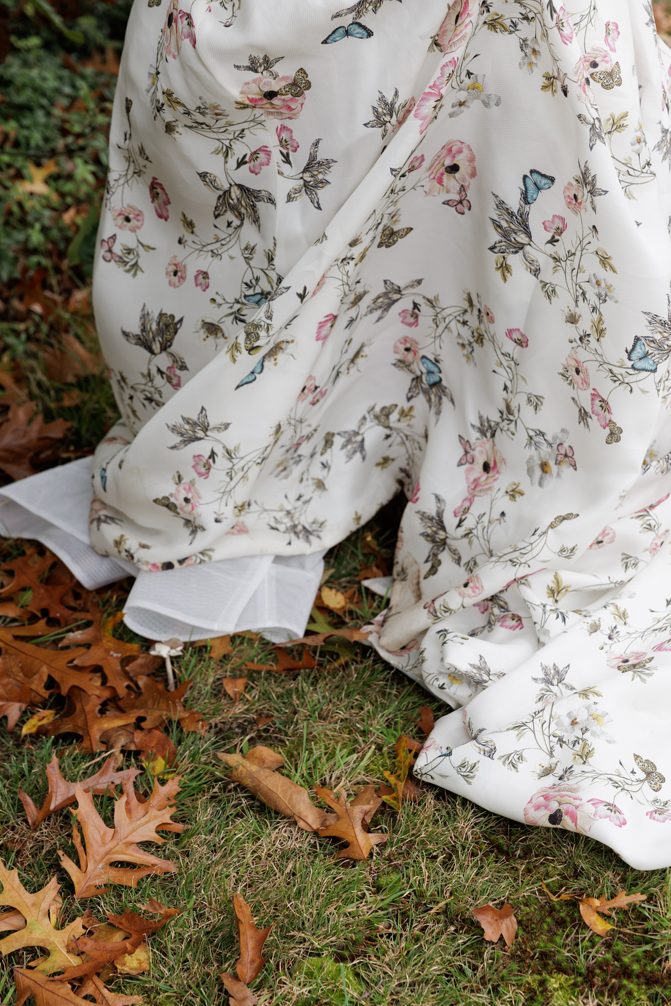 Closeup of the hem of a long floral gown on green grass and brown oak leaves at a backyard wedding in NJ