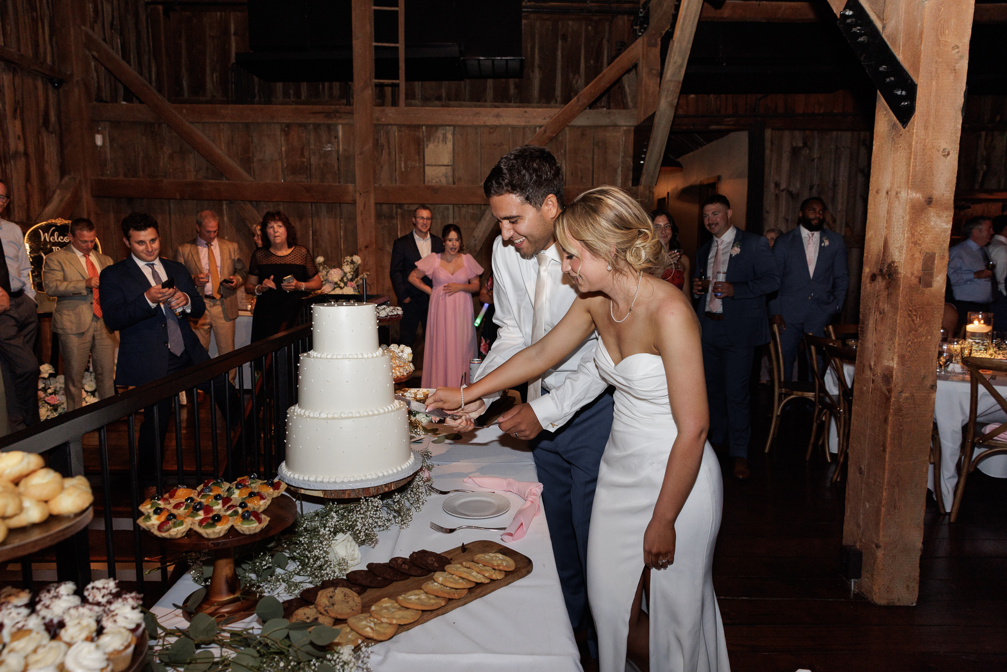 Elegant bride and groom cut a three layered wedding cake during a reception at Farm at Eagles Ridge in Lancaster, PA