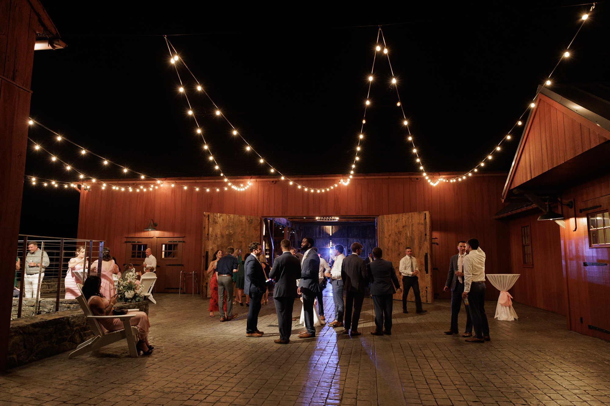 Guests gather under strings of cafe lights on a patio near the Barn during a wedding at Farm at Eagles Ridge in Lancaster, PA