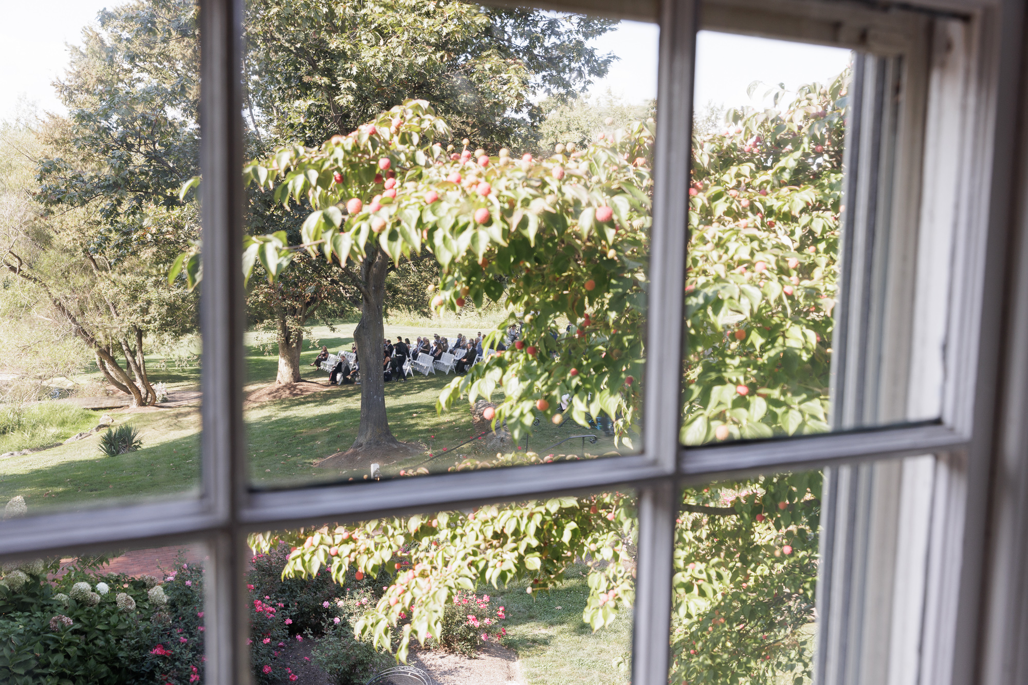 View through window panes at the Farm at Eagles Ridge of guests seated for a wedding ceremony on a lawn at the Farm at Eagles Ridge in Lancaster, PA