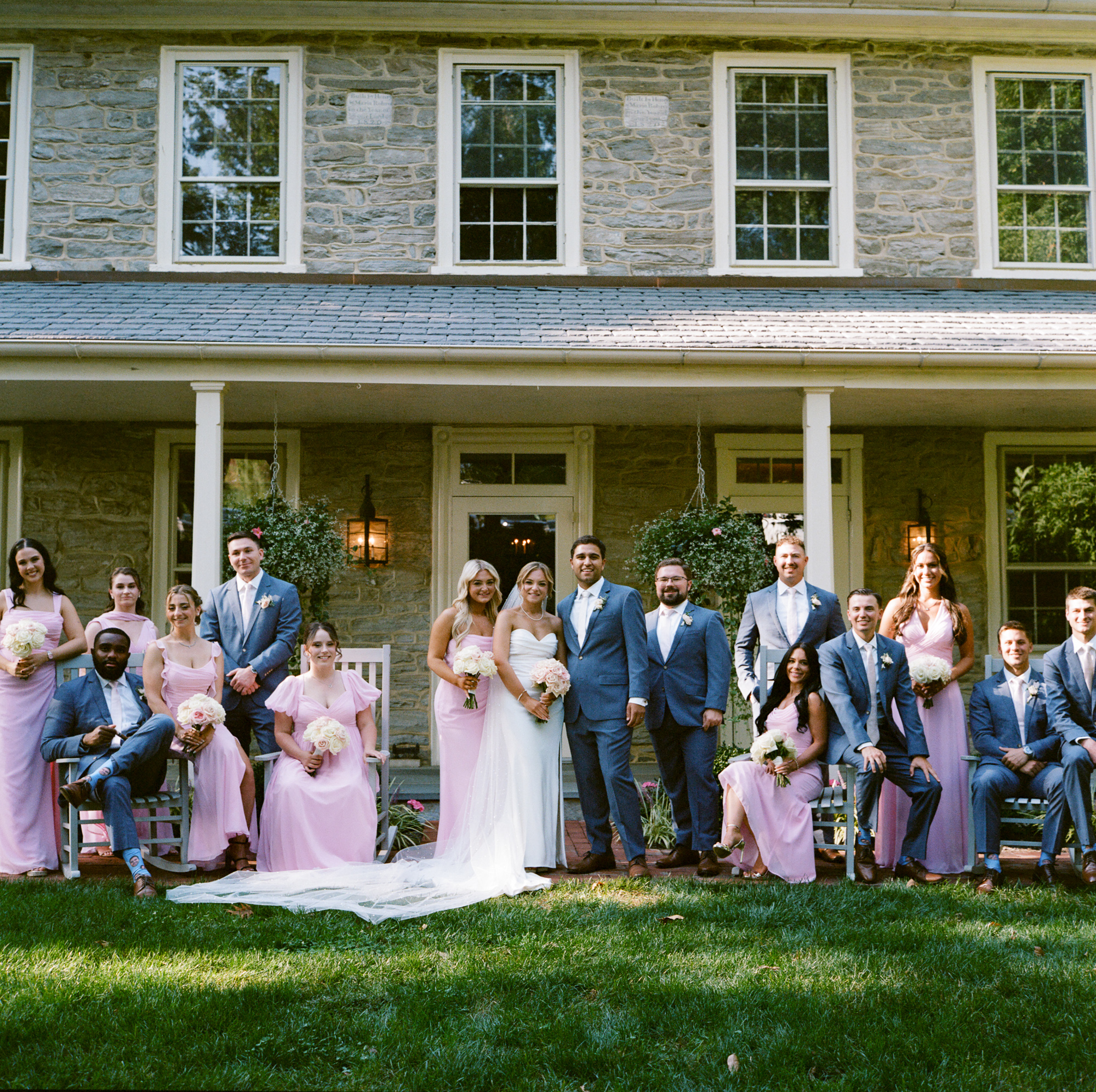 A large wedding party of strike a formal pose in front of the Farmhouse during a summer wedding at Farm at Eagles Ridge in Lancaster PA