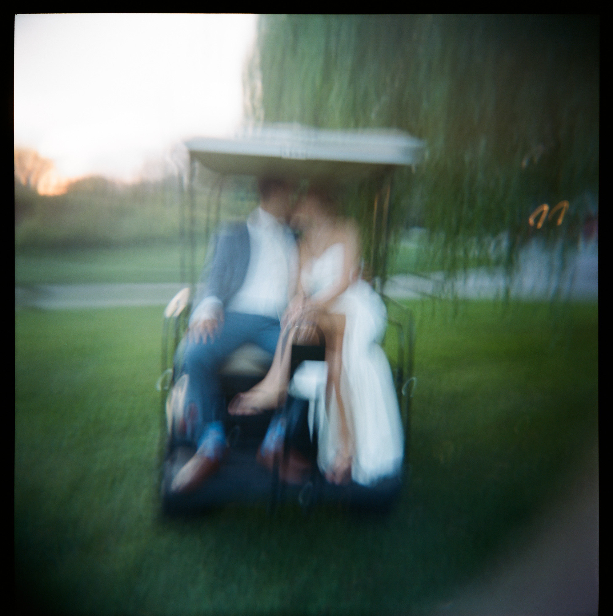 Blurry film photo taken with a Holga camera of a bride and groom riding on the back of a golf cart at Farm at Eagles Ridge in Lancaster, PA