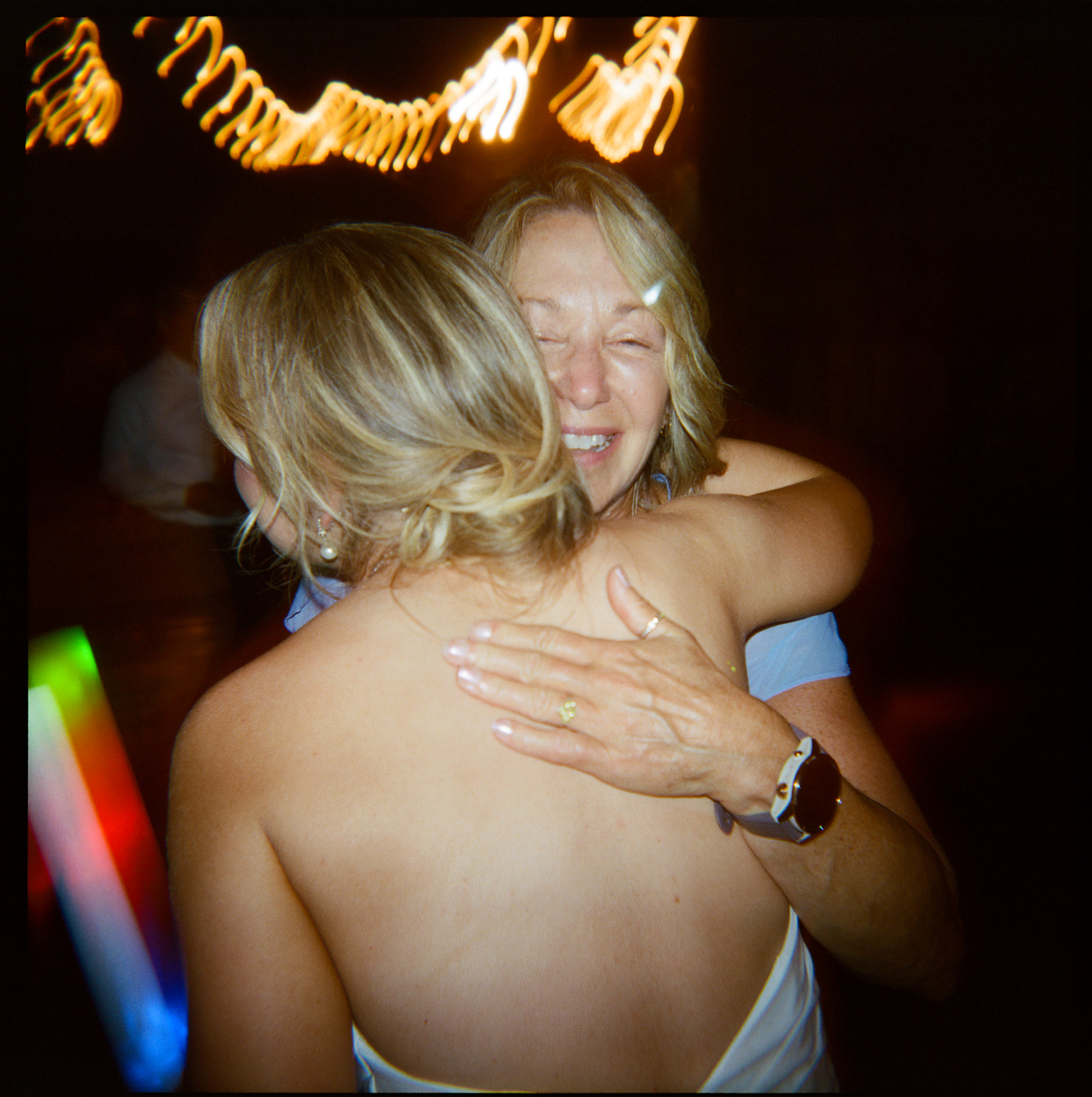 Bride holding a light stick given by a wedding dj hugs a friend on the dance floor at Farm at Eagles Ridge in Lancaster, PA
