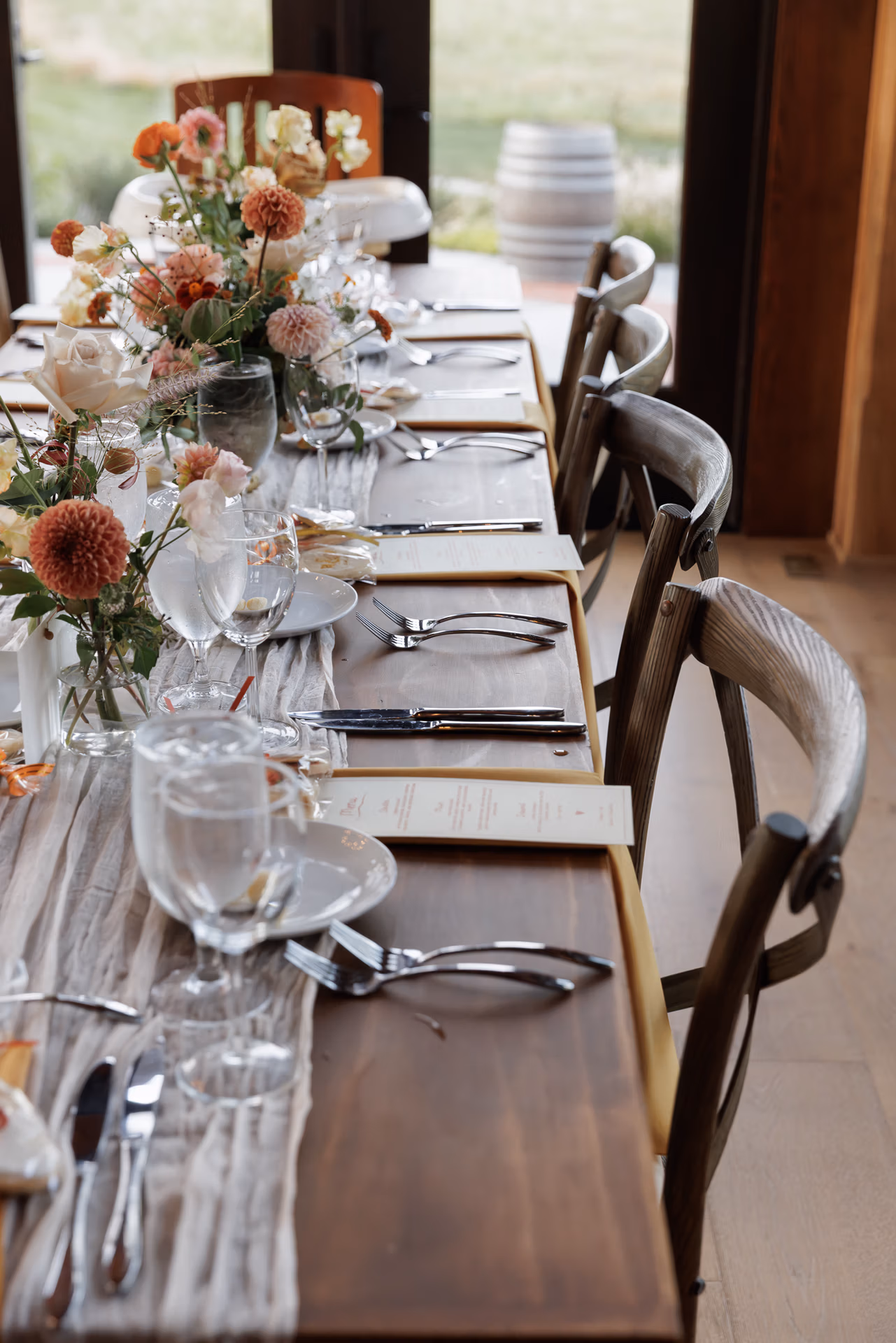 Rustic elegant table settings with orange, coral and deep red fall flower arrangements at a Northridge Barn at Woolverton Inn wedding reception