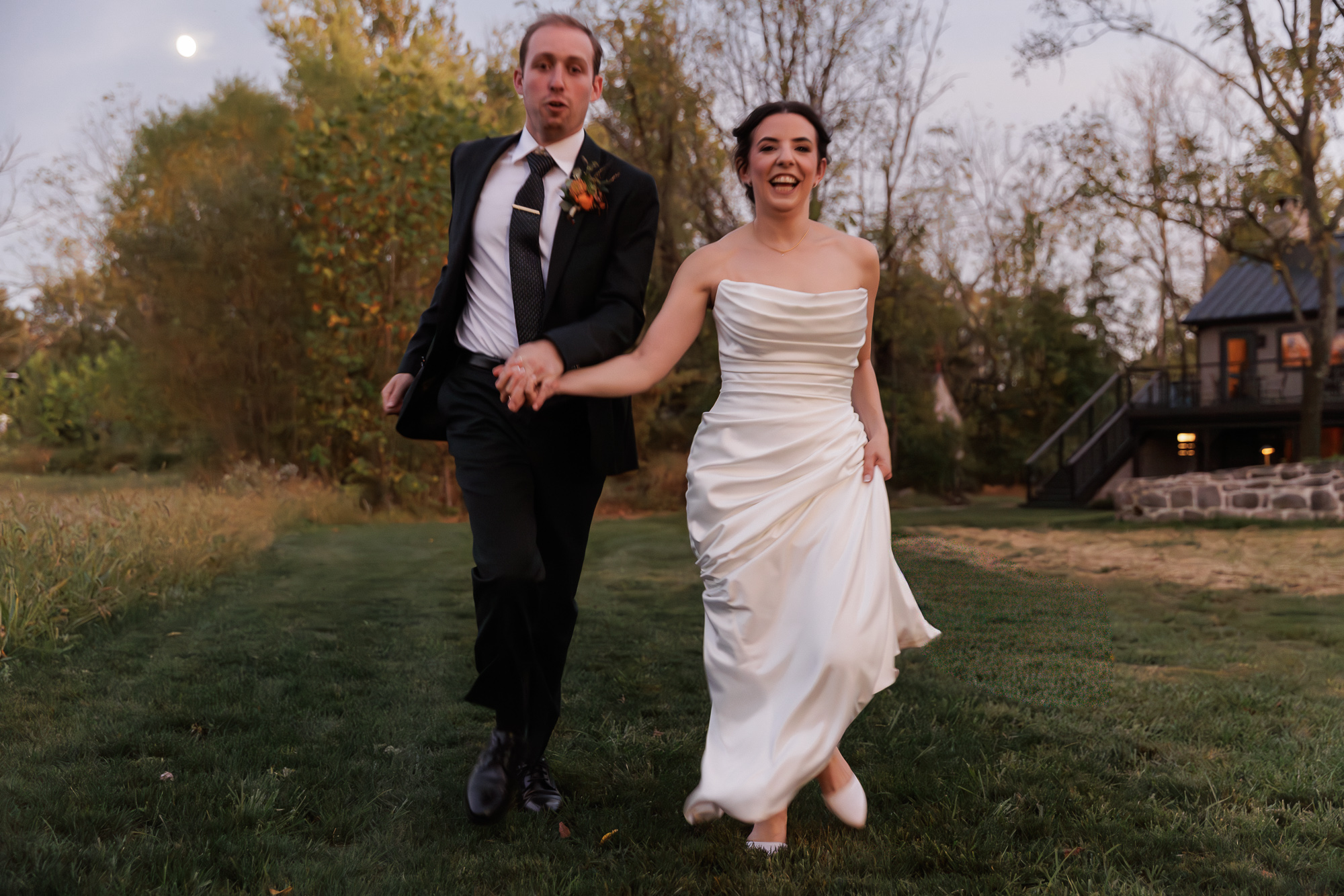 Elegant bride and groom run through a field during blue hour at their Northridge Barn at Woolverton Inn wedding reception
