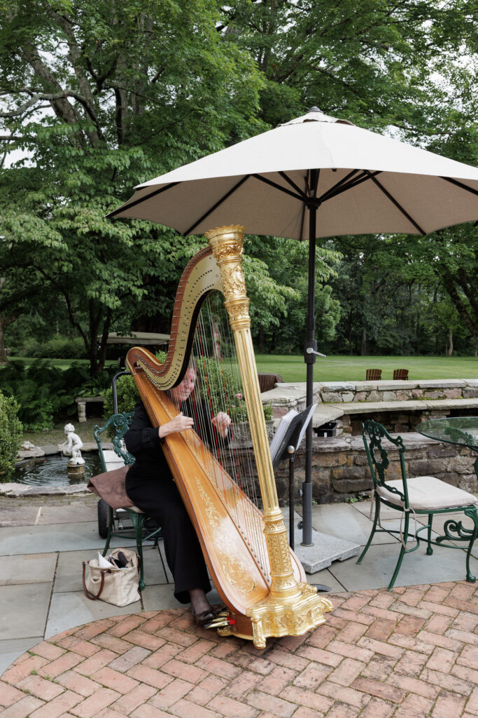 A harpist on a brick and flagstone patio at the Woolverton Inn plays music before a wedding ceremony