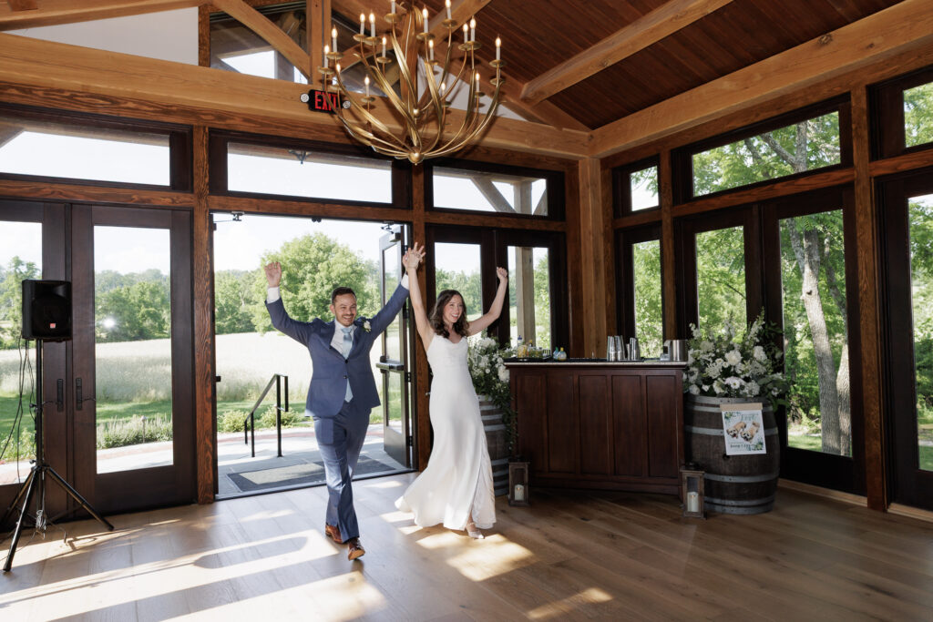 A bride and groom clasp raised hands as they enter their wedding reception in the Northridge Barn at the Woolverton Inn 