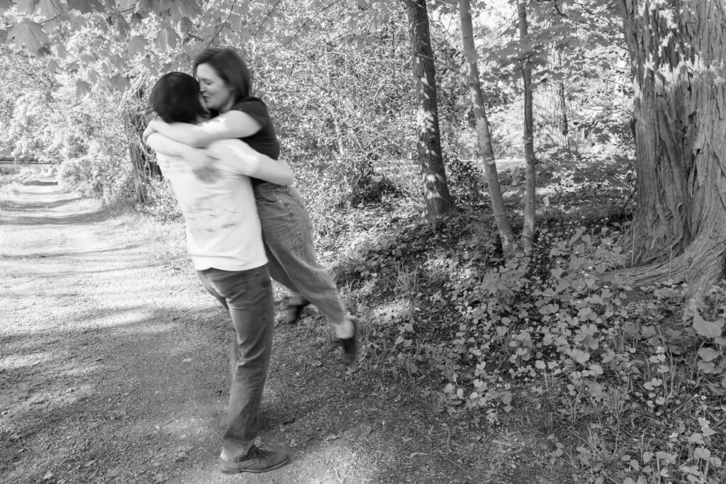 A black and white slightly blurry image of a man in a t-shirt and black jeans picking up a woman with a dark t-shirt and light jeans and swinging her around
