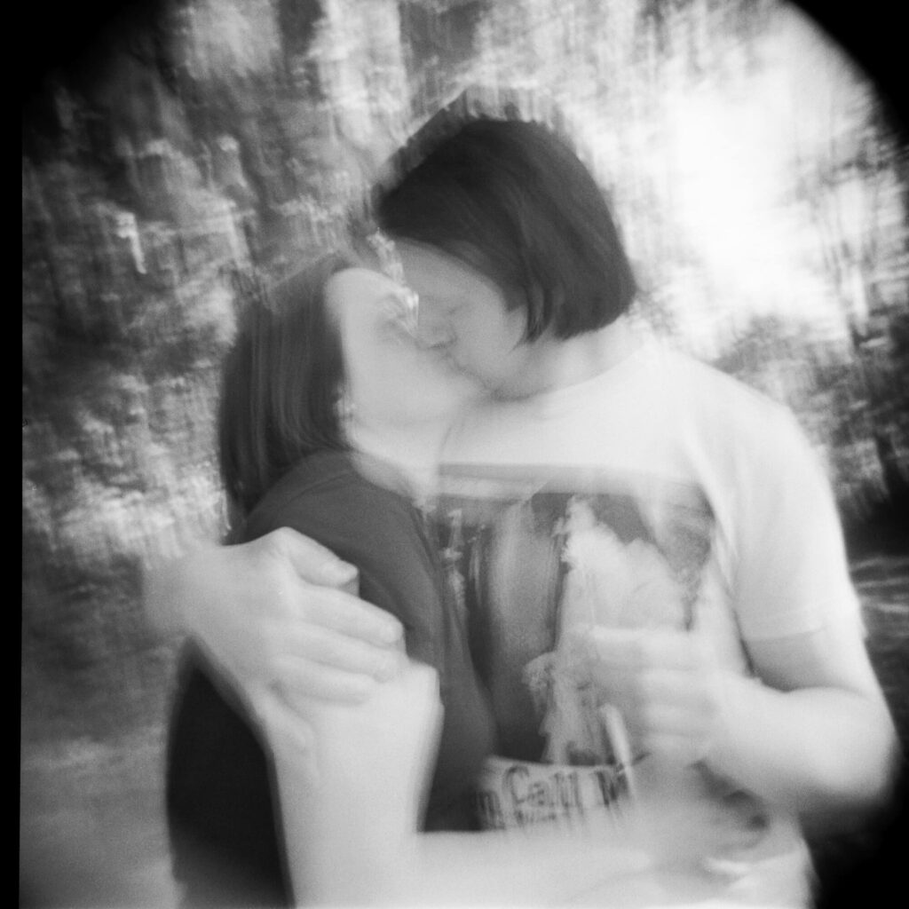 a dreamy, blurry black and white image of a man with dark hair kissing a woman with dark hair