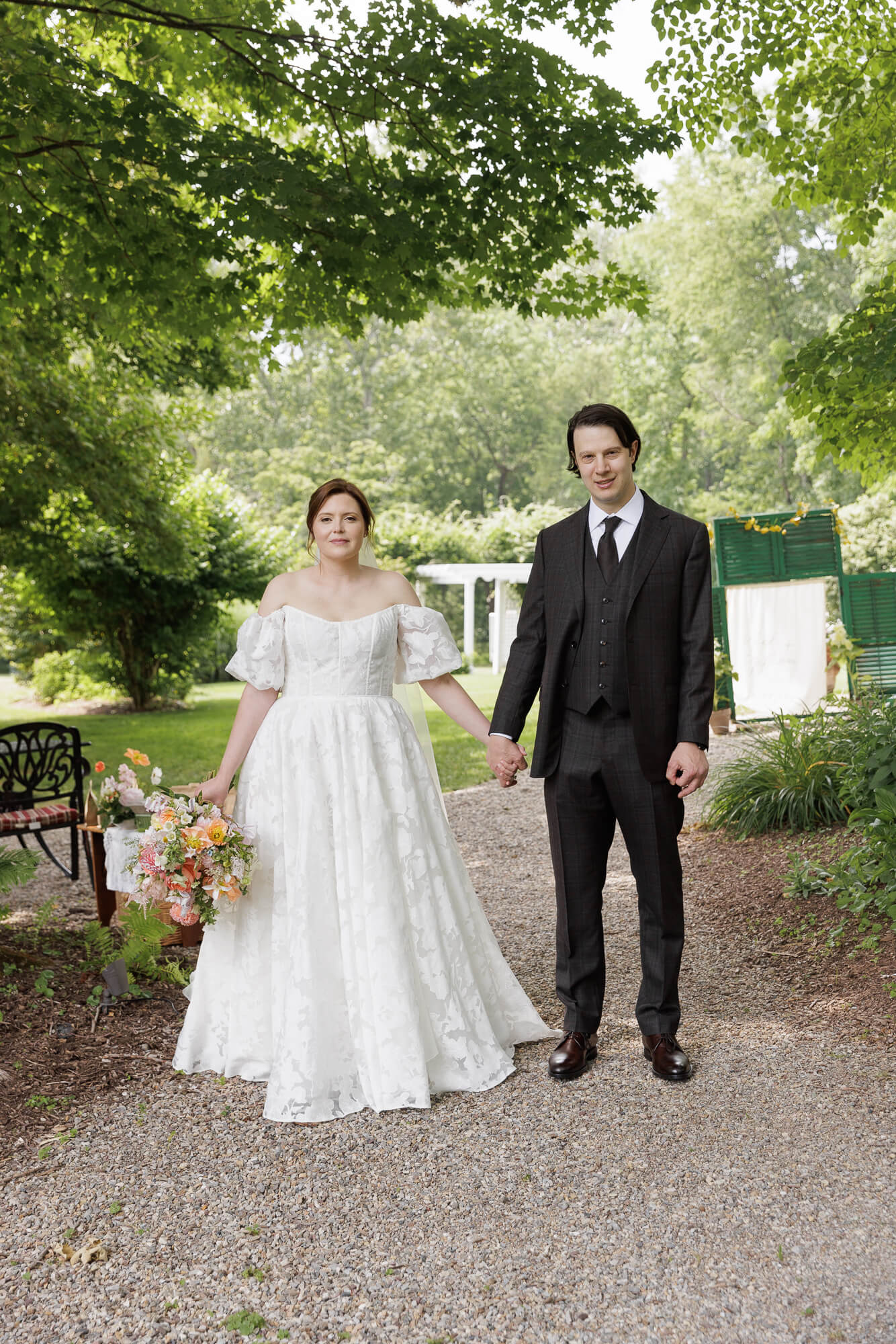 A bride and groom pose very formally, facing the camera, under a large shady tree at the Woolverton Inn