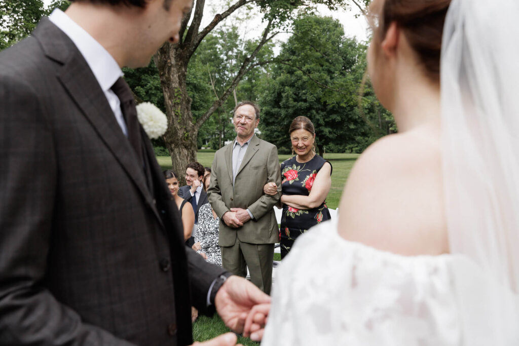 A bride and groom frame the groom's parents, who standing to face the couple