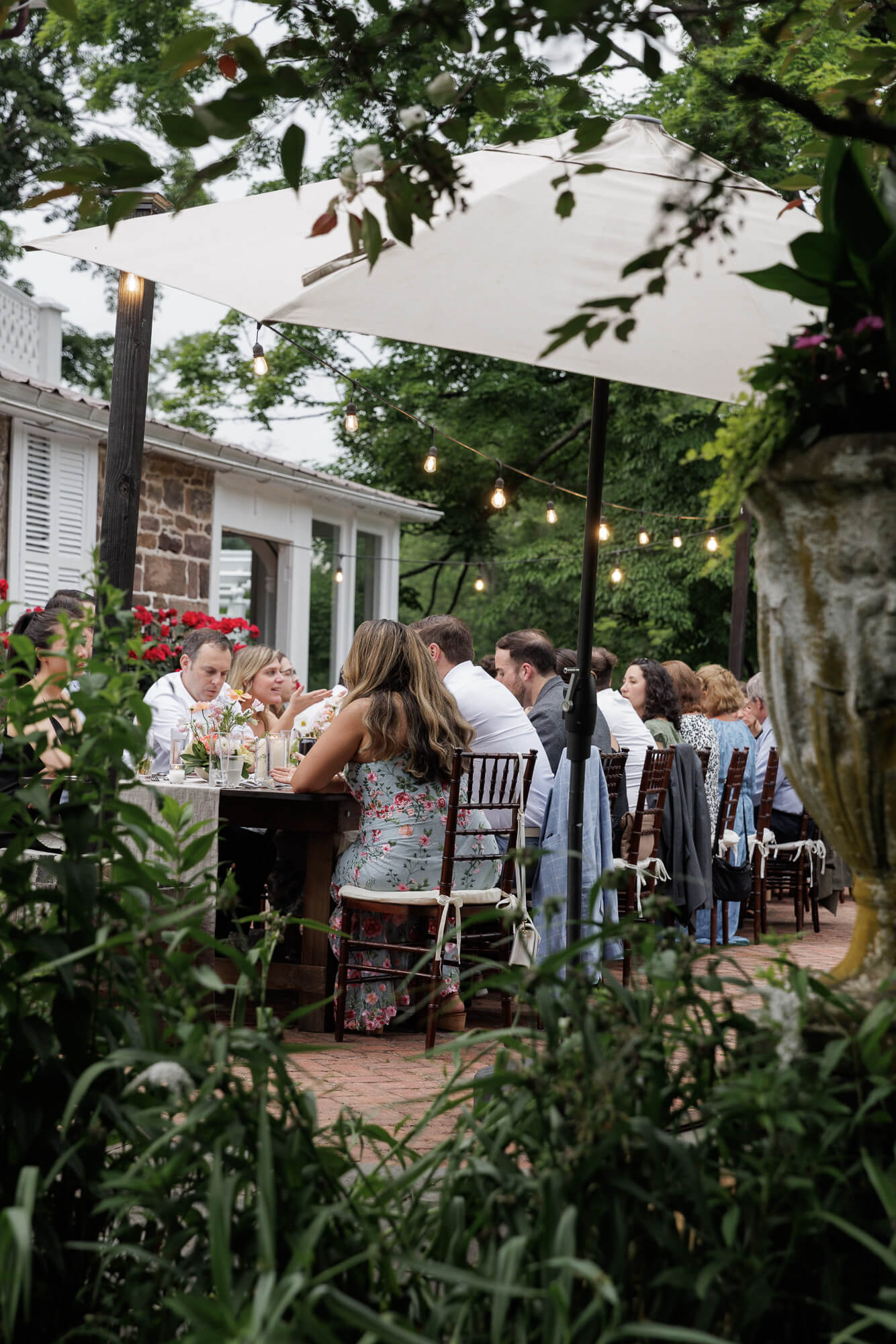 Guests enjoy dinner at one long rustic farmhouse table at an outdoor micro wedding reception