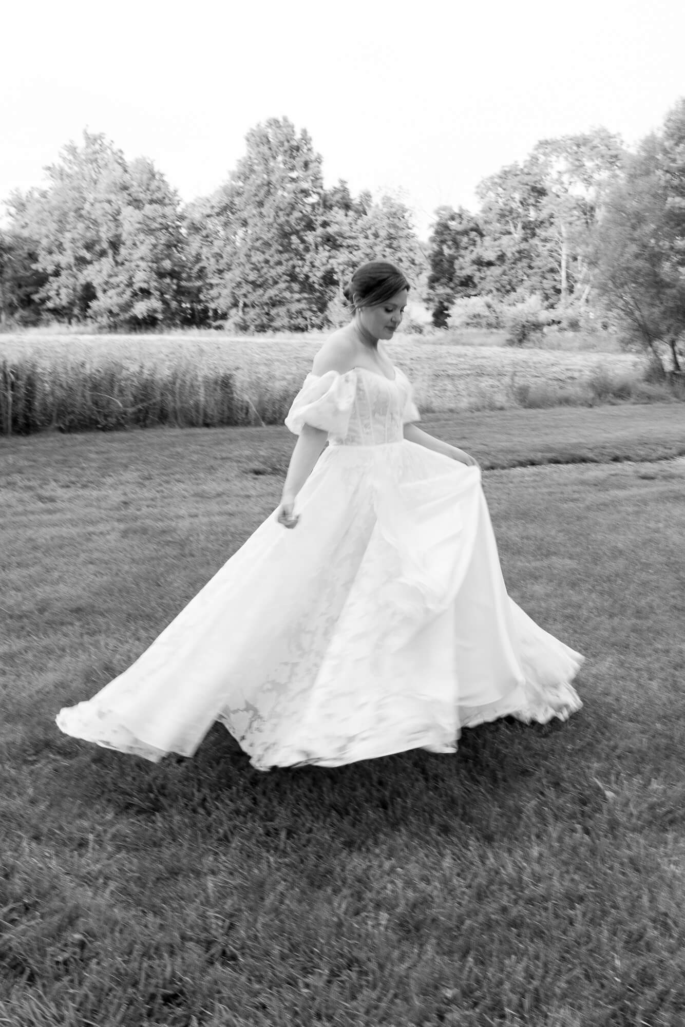 Black and white image of a bride twirling in a long gown on an open lawn
