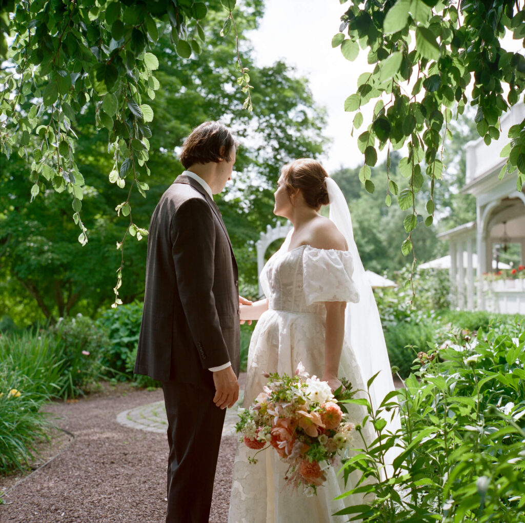 A film photograph of a bride and groom in formal attire from behind, in the garden at the Woolverton Inn
