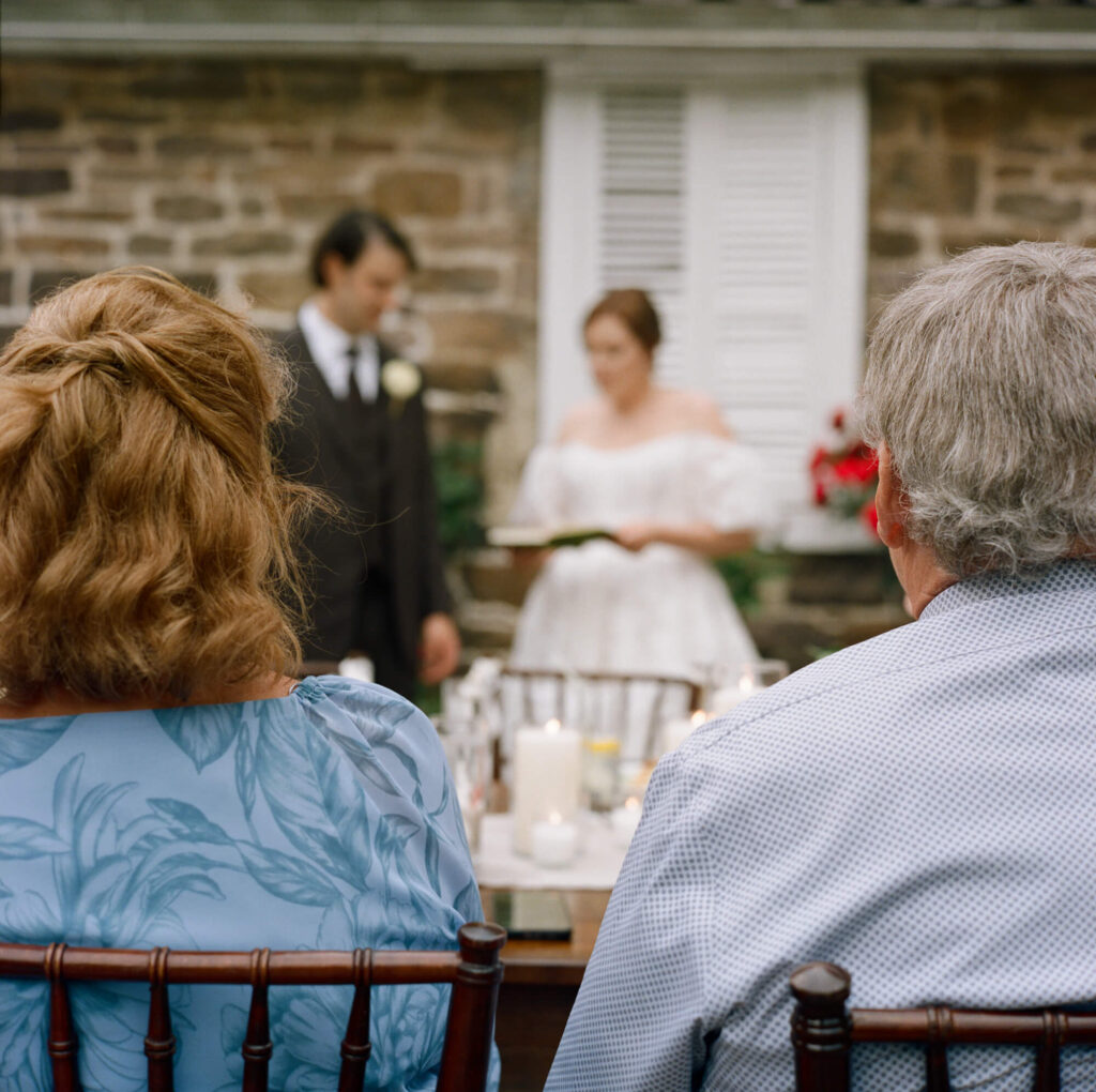 Film photo of a groom and bride welcoming guests to their micro wedding reception as the bride's parents look on