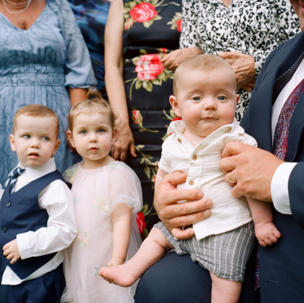 film photograph of two toddlers and a baby seated on a parent's knee