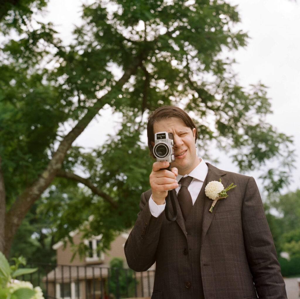 Film photograph of a groom in a brown three piece suit shooting with a Camp Snap 8mm camera