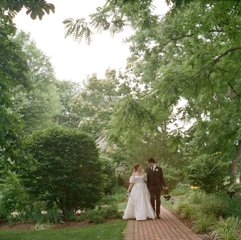 Film photo of bride and groom walking through trees at the Woolverton Inn